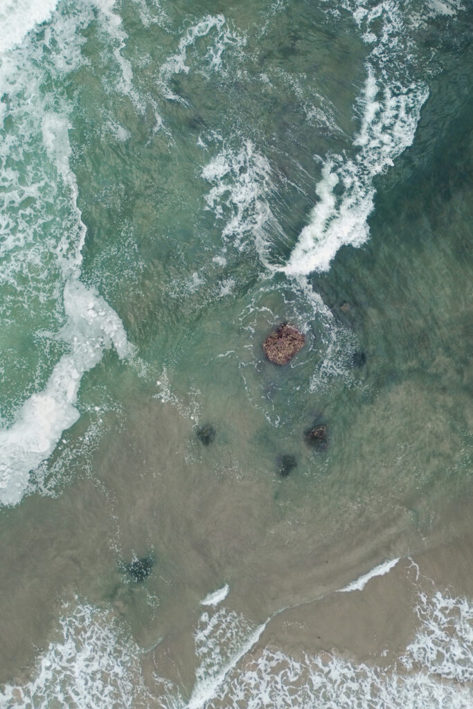 Aerial view of ocean waves and rocky shore during an Oregon Coast elopement, with soft teal water.