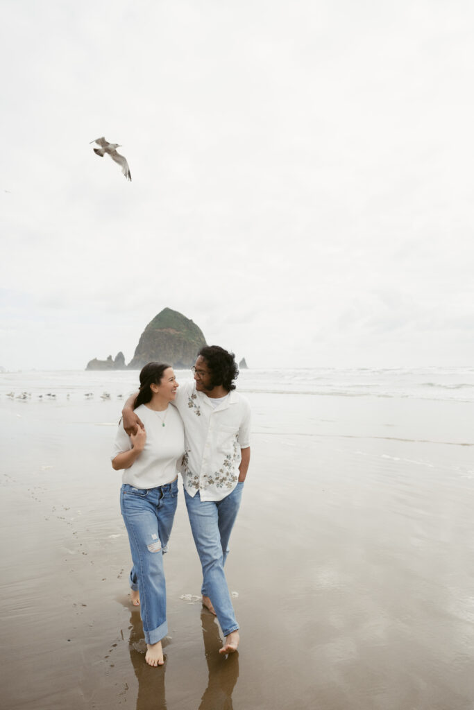 Couple walking barefoot along the beach during their Oregon Coast elopement, smiling with Haystack Rock behind.