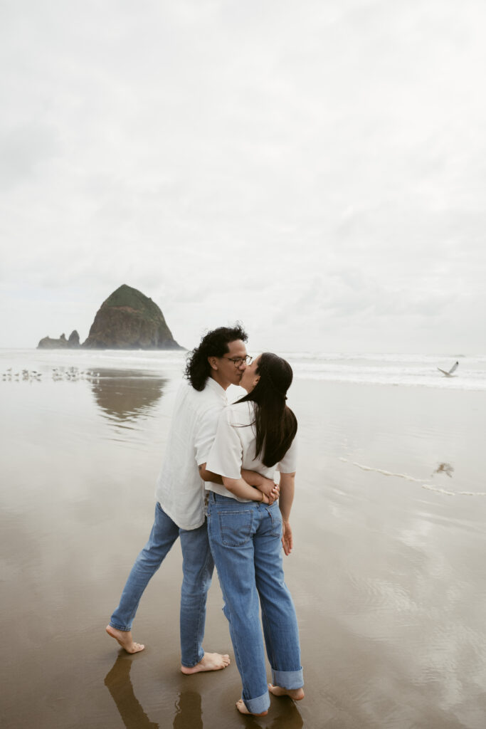 Couple kissing on the shoreline during their Oregon Coast elopement, with Haystack Rock in view.