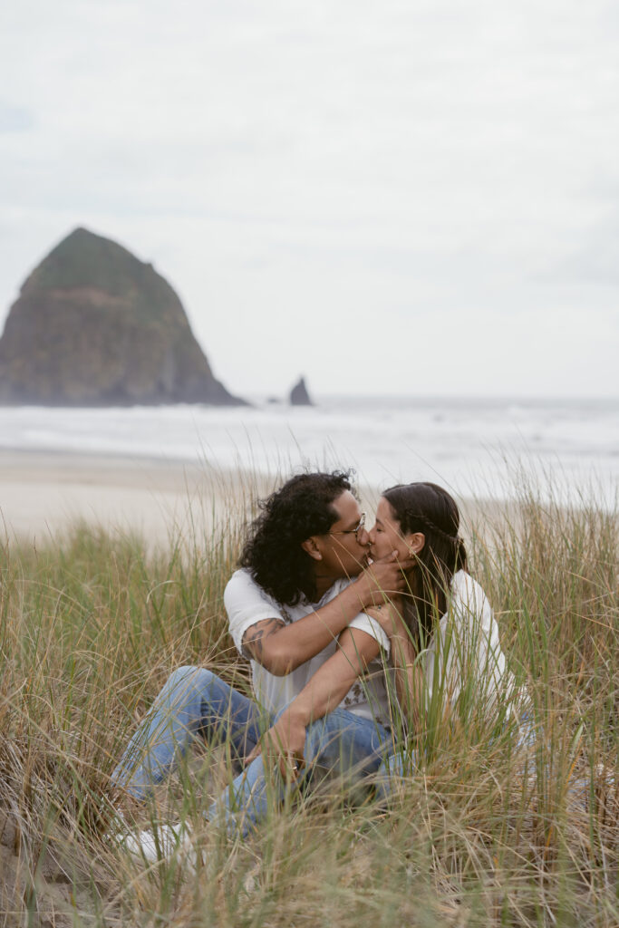 Couple kissing in tall beach grass during their Oregon Coast elopement, with Haystack Rock behind them.