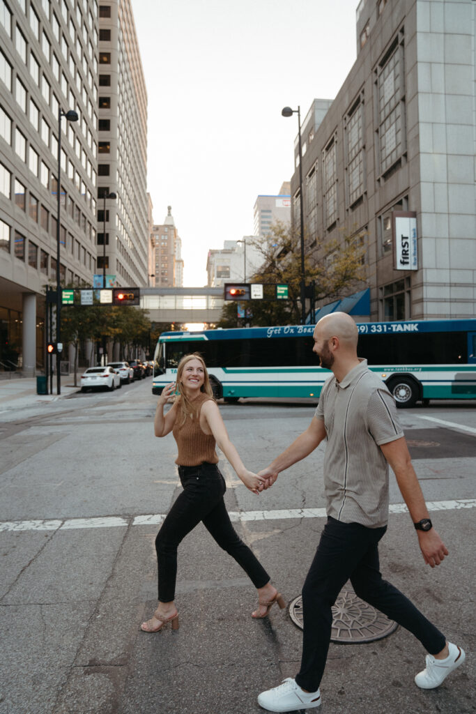 engagement-photo-tips Couple crossing a downtown Cincinnati street holding hands, captured during their urban engagement session as part of creative engagement photo tips.