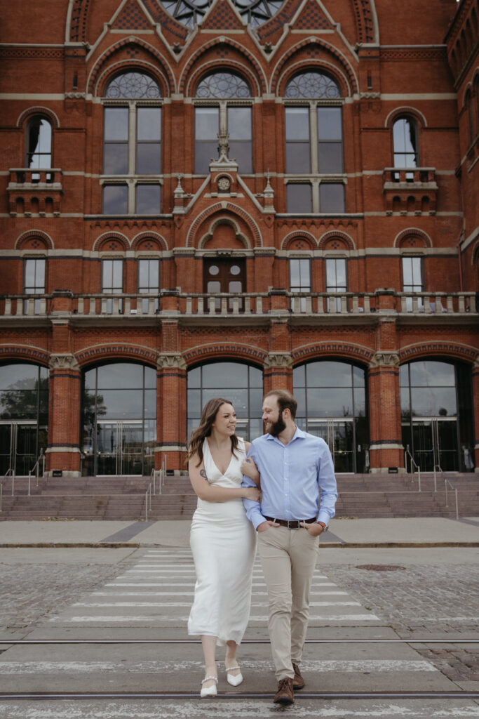 engagement-photo-tips Couple walking arm in arm in front of Cincinnati’s historic Music Hall during their engagement session, captured as part of their engagement photo tips experience.
