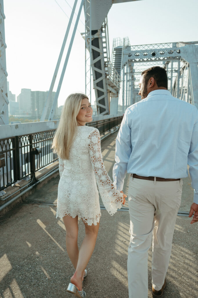 engagement-photo-tips Couple walking hand in hand across a Cincinnati bridge during their engagement session, captured as part of creative engagement photo tips.