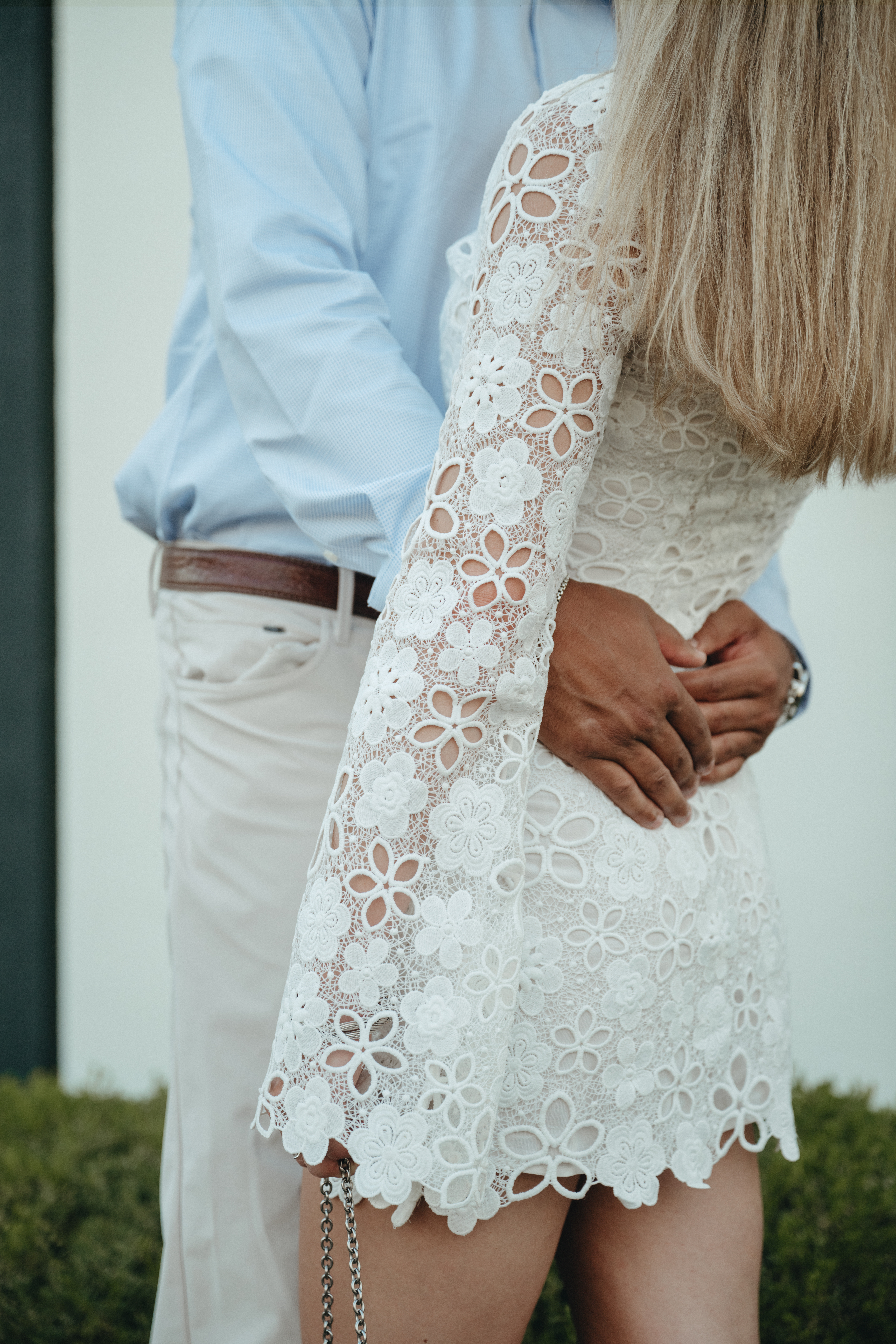 engagement-photo-tips Close-up of a couple embracing, with the woman wearing a white lace floral dress and the man in a light blue shirt and cream pants.