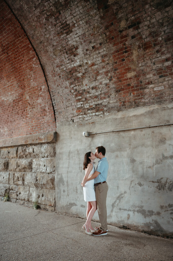 engagement-photo-tips Couple sharing a kiss under a brick and stone archway during their Cincinnati engagement session, captured as part of creative engagement photo tips.