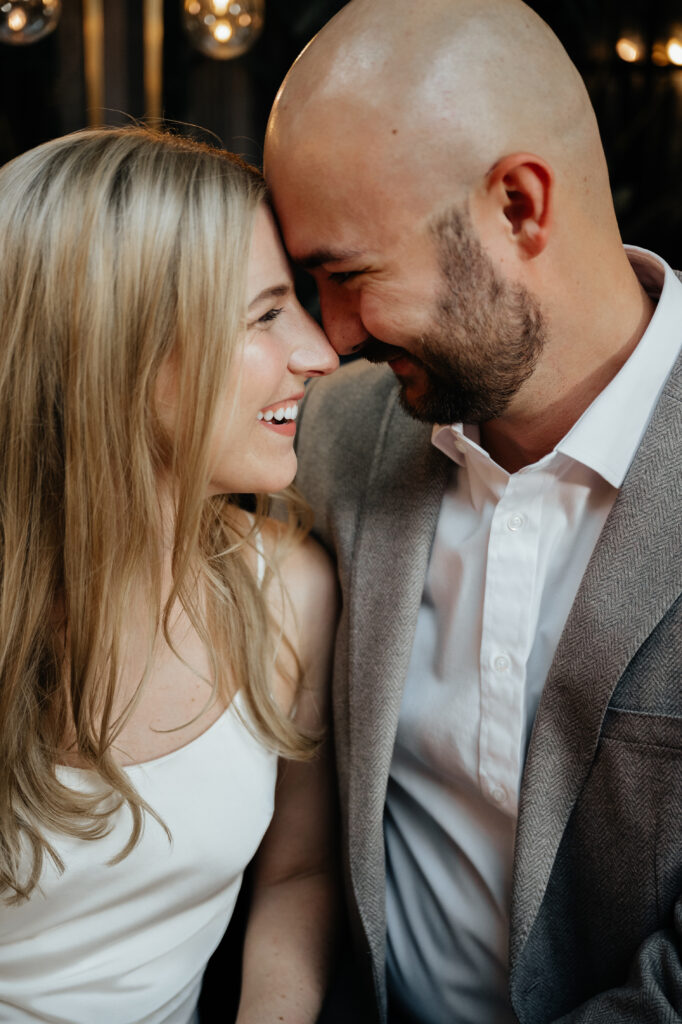 engagement-photo-tips Couple smiling and leaning their foreheads together, sharing a joyful and intimate moment in a warmly lit setting.