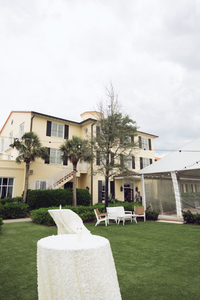 Outdoor cocktail hour setup on the lawn at The King and Prince Resort with white linen-covered tables and seating in front of a yellow historic building.