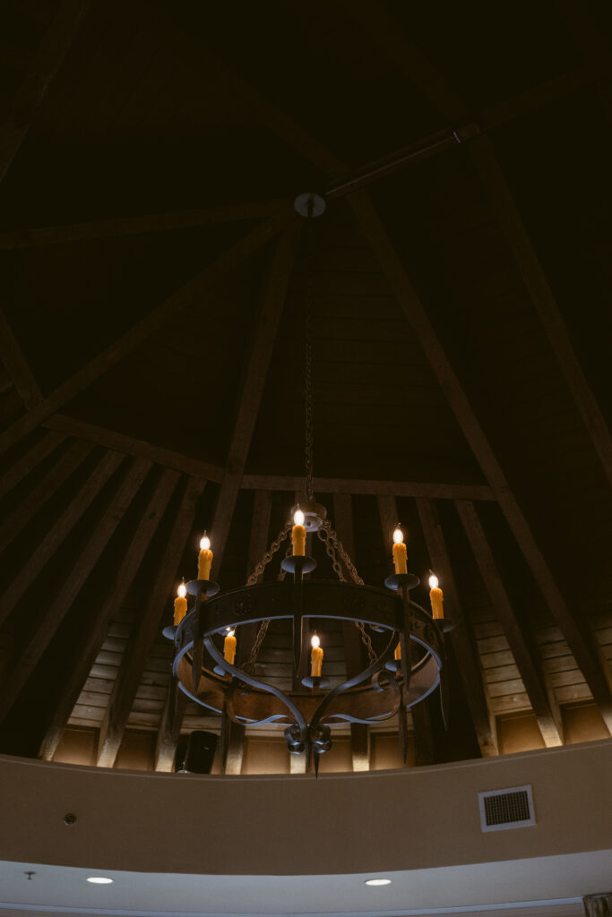 Rustic chandelier with glowing candles hanging from a vaulted wood ceiling inside The King and Prince Resort during a Georgia wedding celebration.