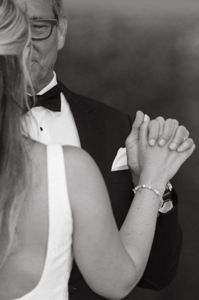 Black and white photo of bride dancing with her father, holding hands during a sweet moment.