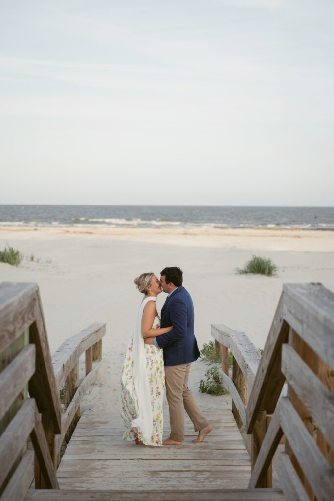Bride and groom share a kiss at the end of a wooden boardwalk leading to the beach during their Georgia wedding on St. Simons Island.