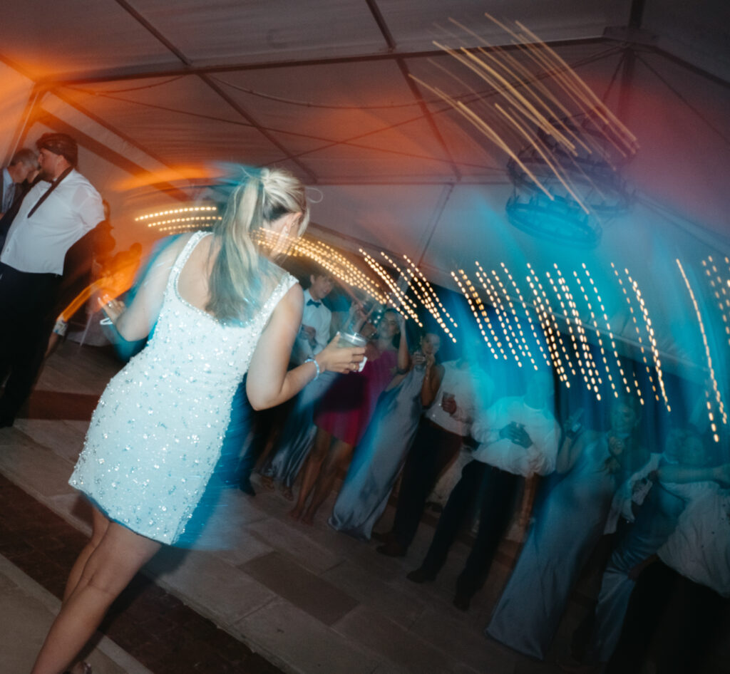 Guest in a sparkly mini dress dances under twinkle lights at a lively wedding reception.