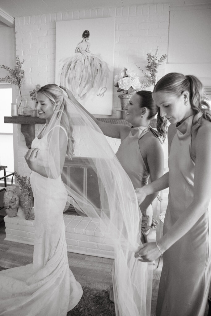 Bride smiling as her bridesmaids help adjust her veil in a cozy cottage setting before her Georgia wedding ceremony.