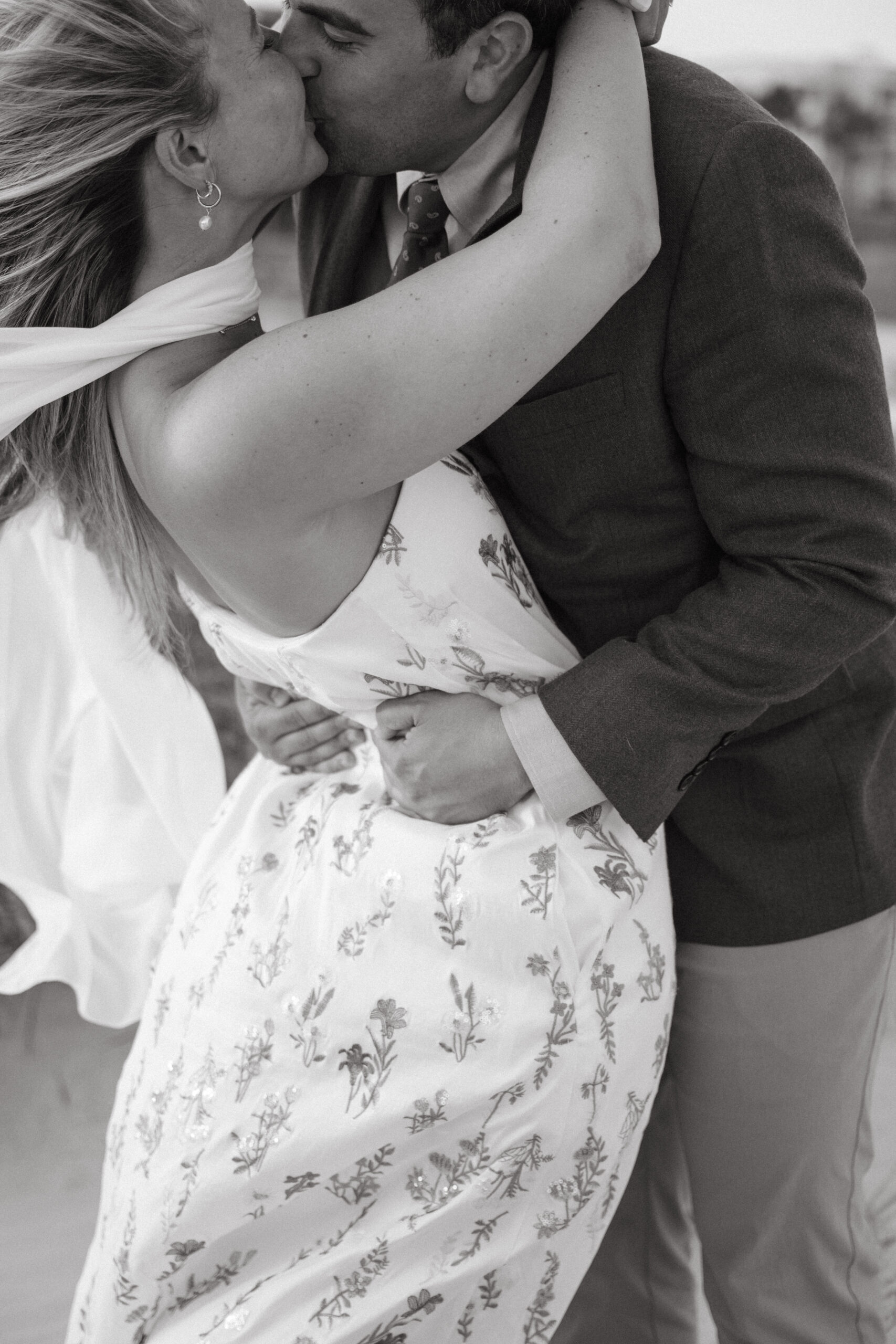 Black and white close-up of a couple sharing a kiss during their Georgia wedding, with the bride in a floral dress and wind-blown scarf.