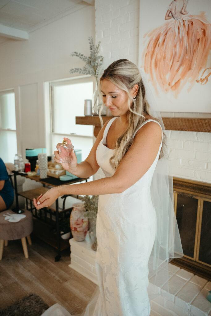 Bride in a white fitted gown applying perfume while getting ready for her Georgia wedding in a cozy cottage room.