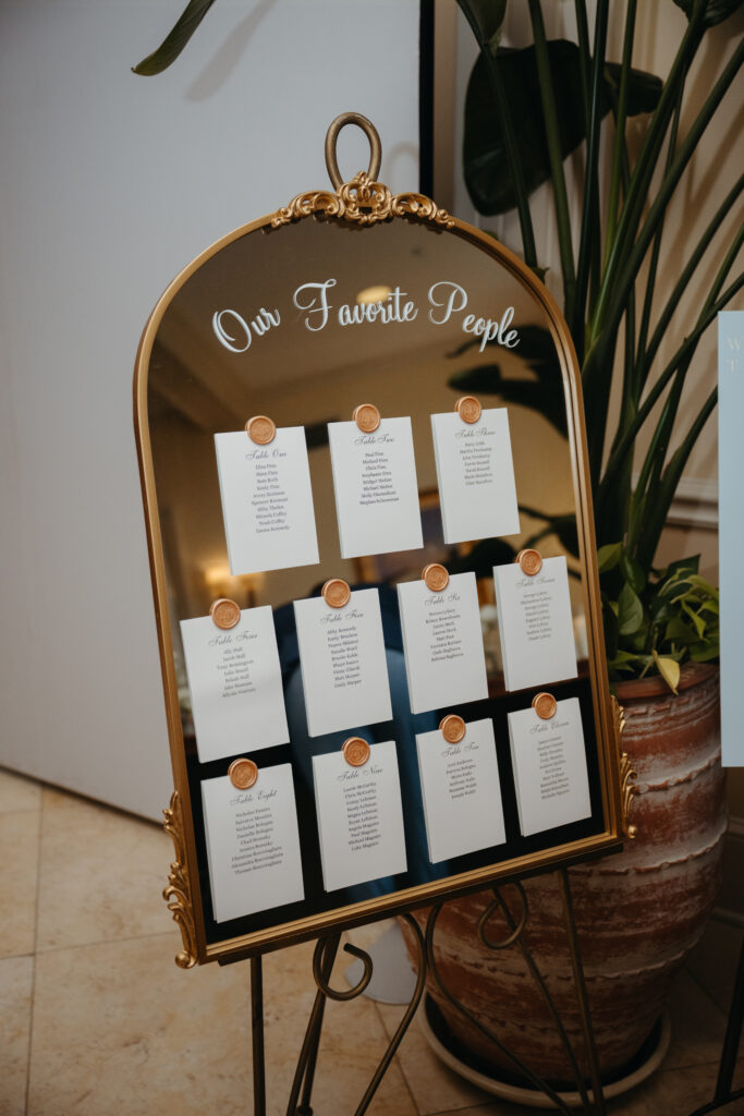 Elegant gold-framed mirror seating chart titled "Our Favorite People" with guest lists for each table.