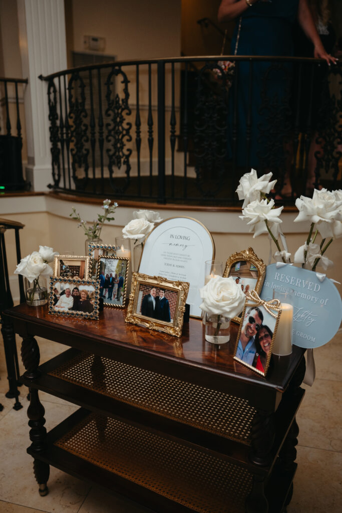 Memorial table with framed photos, white roses, and candles honoring loved ones at the wedding.