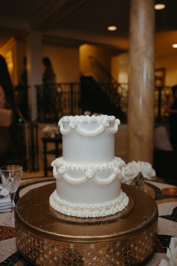 Elegant three-tier white wedding cake with piped details on a gold mosaic cake stand.