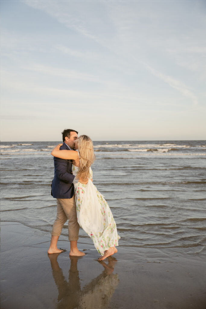 Bride and groom embrace barefoot in the shallow tide during their Georgia wedding, with soft waves and golden light reflecting around them.