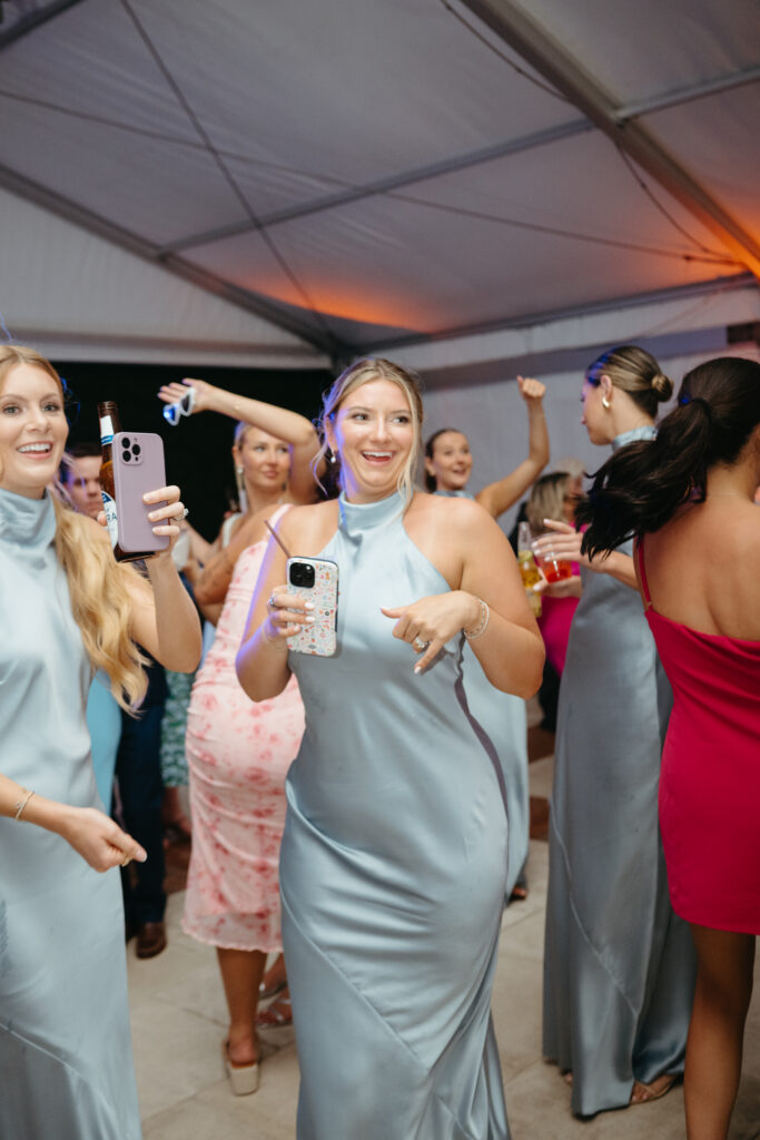Bridesmaids in satin blue dresses dance and record videos during the wedding reception.