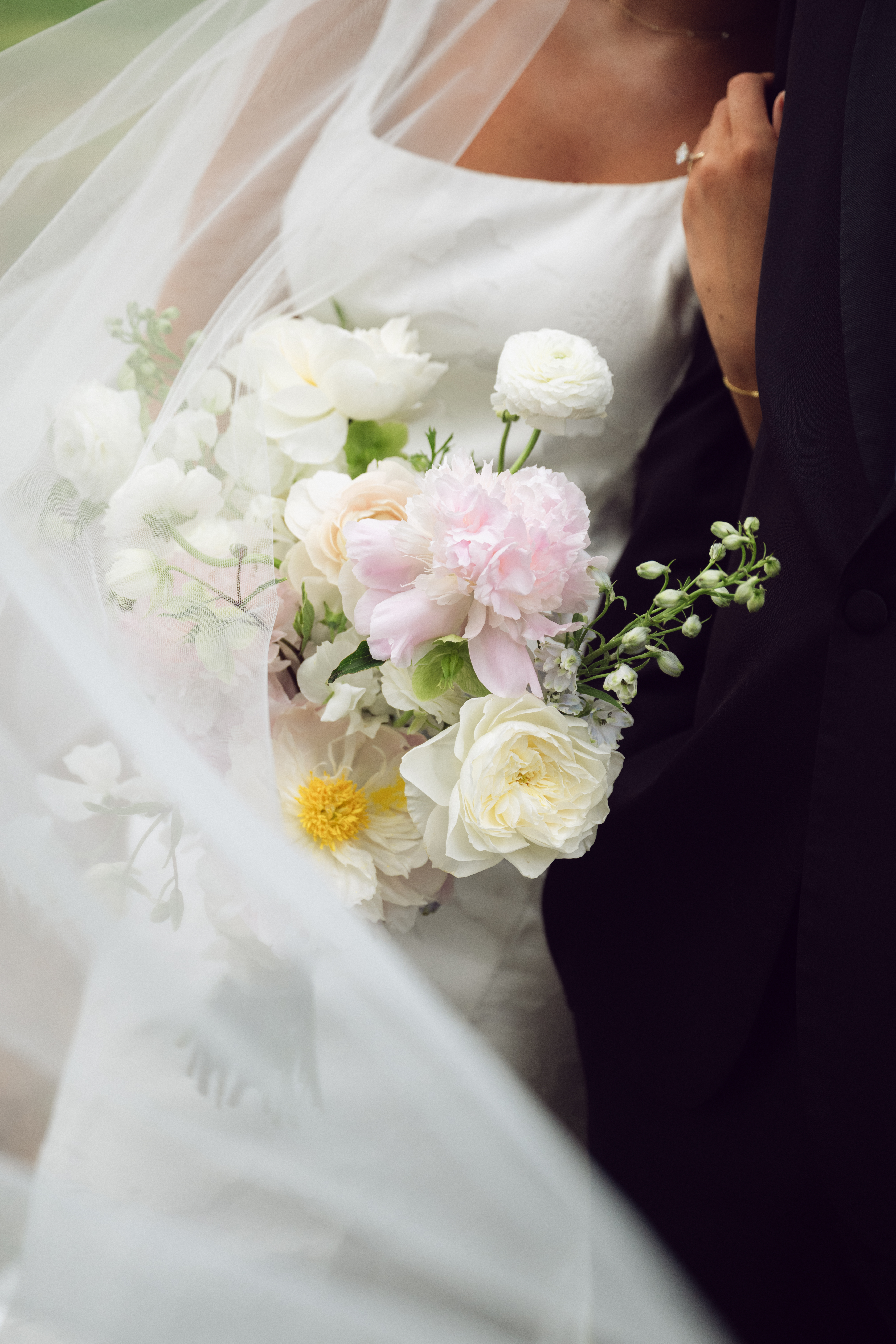 Close-up of a bride holding a pastel bouquet of roses, peonies, and ranunculus, with her veil softly blowing in the breeze during a romantic Georgia wedding.