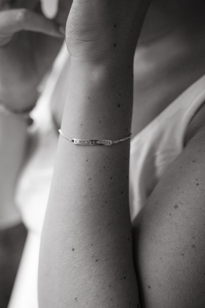 Close-up of the bride’s wrist showing a delicate silver bracelet engraved with a meaningful message, captured in soft black and white during her Georgia wedding morning.