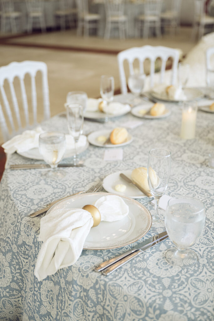 Elegant place settings with gold napkin rings and lace-patterned linens at the reception.