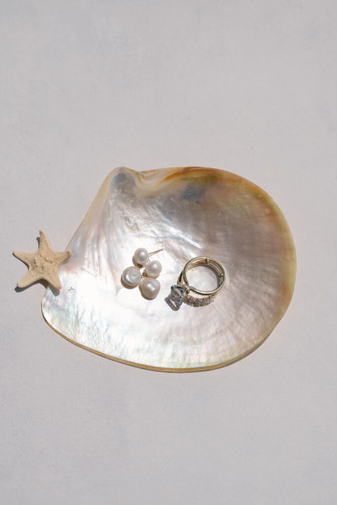 Close-up of wedding rings and pearl earrings displayed on a mother-of-pearl shell with a tiny starfish, styled for a coastal Georgia wedding.