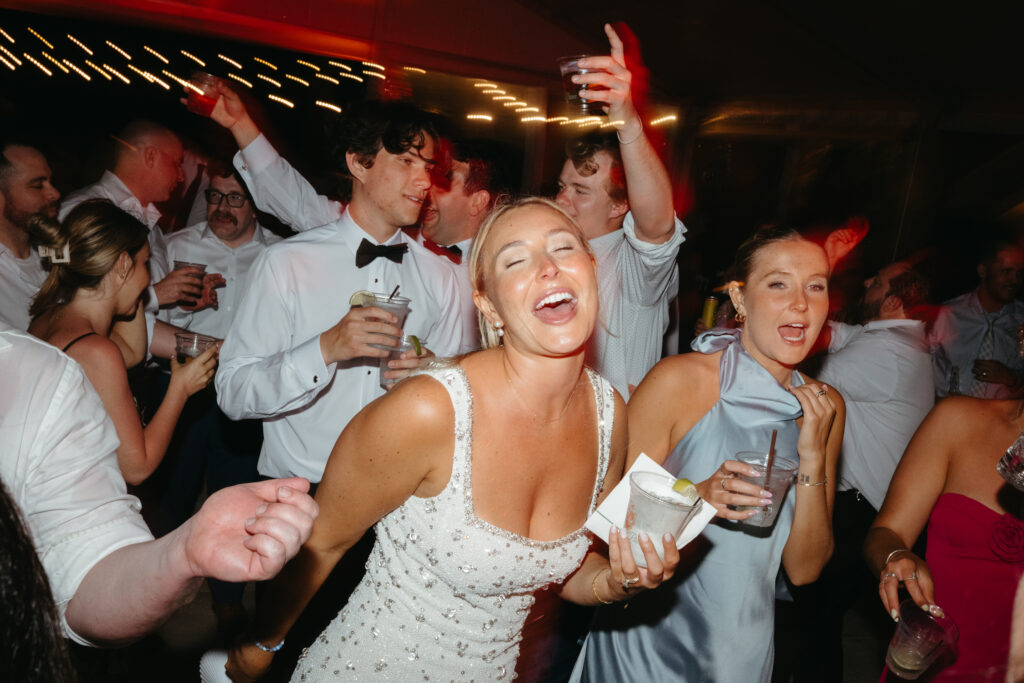 Guests dancing and celebrating under colorful lights during the wedding reception, with drinks in hand and joyful expressions.