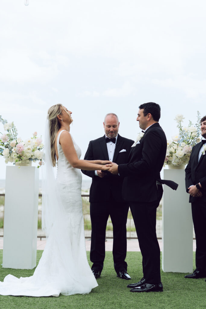 Bride and groom exchange vows during outdoor ceremony, laughing and holding hands at the altar.