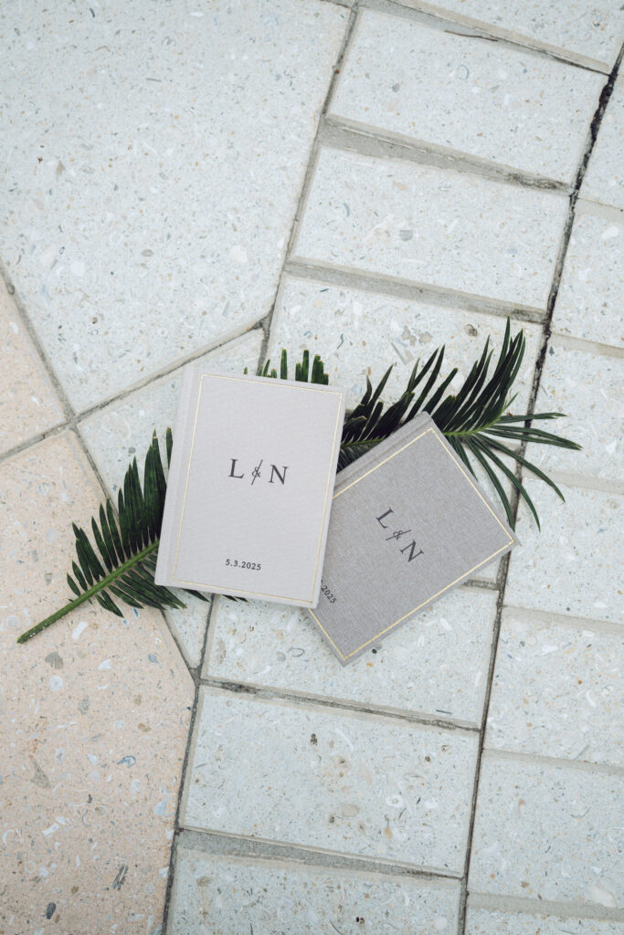 Flat lay of custom linen vow books with gold trim and monogrammed initials, styled with greenery for a beachside Georgia wedding.
