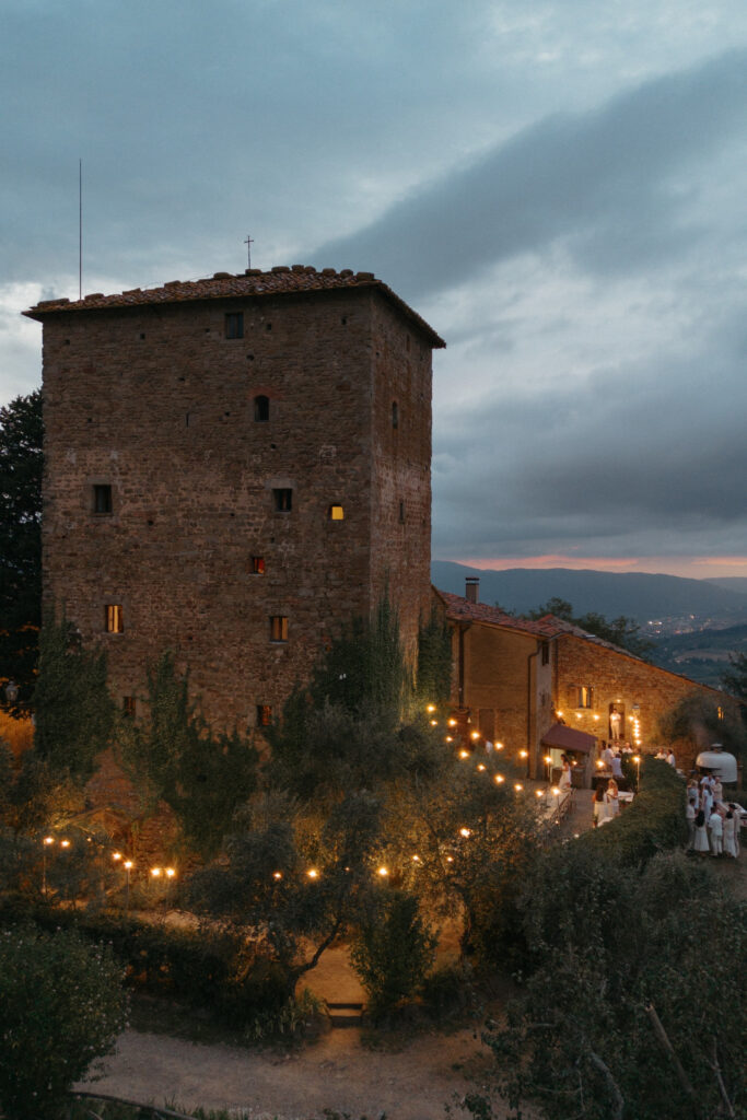 Evening view of a rustic stone villa in the Italian countryside, lit with string lights and surrounded by olive trees — a dreamy setting for getting married in Italy.