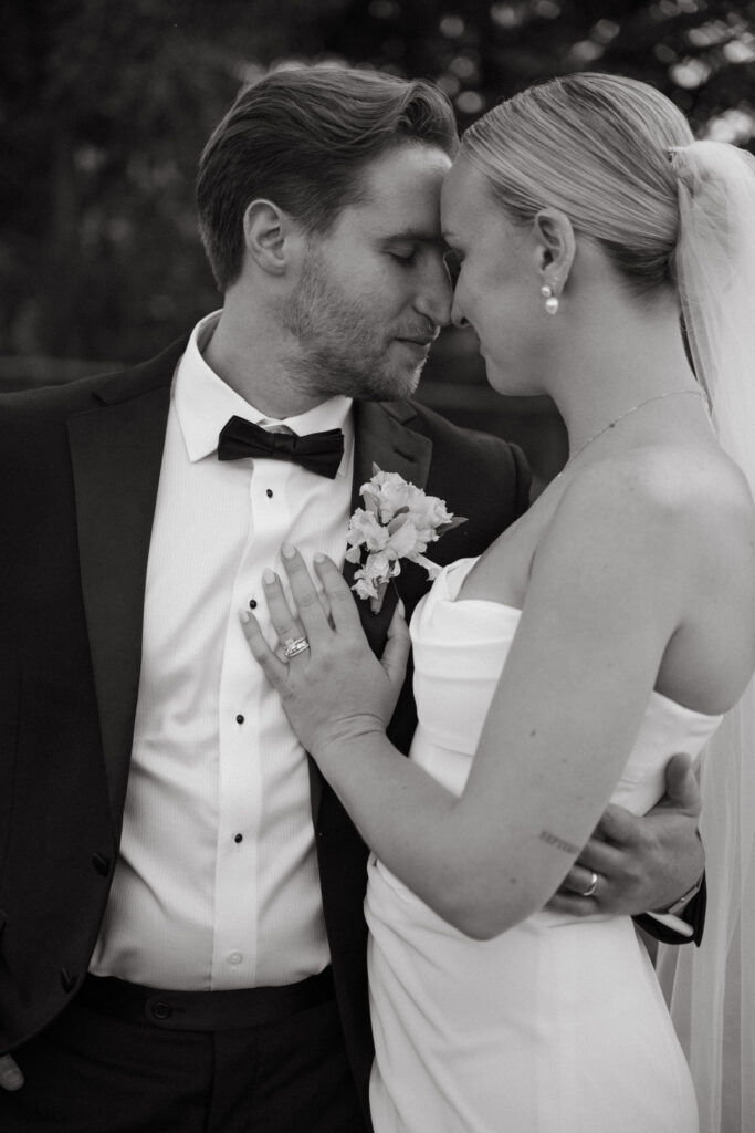 Black and white photo of a bride and groom standing forehead to forehead, eyes closed, sharing an intimate moment on their wedding day.