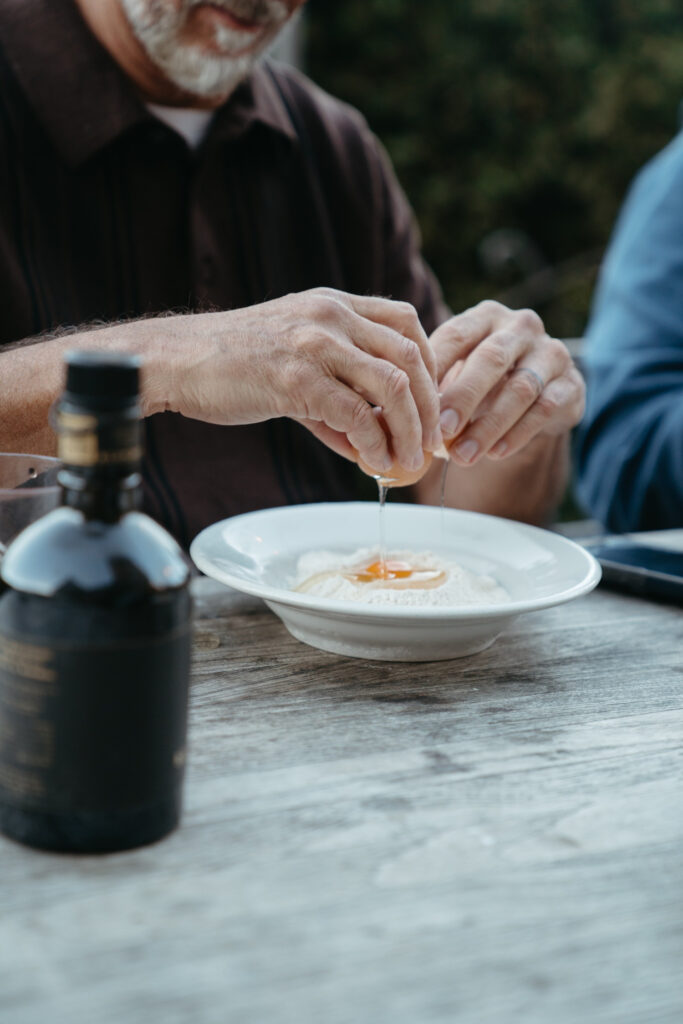 Man cracking an egg into a bowl of flour while preparing fresh pasta outdoors — a hands-on culinary moment often enjoyed while getting married in Italy.
