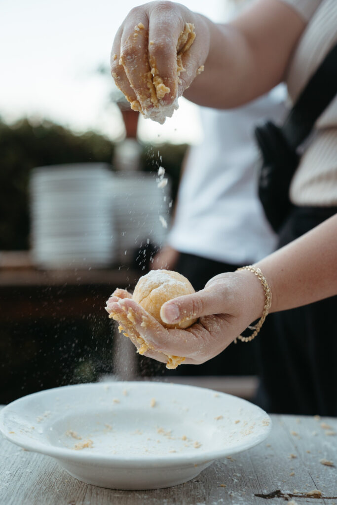 Close-up of hands shaping fresh pasta dough over a bowl, with flour falling — a hands-on culinary moment often shared while getting married in Italy.