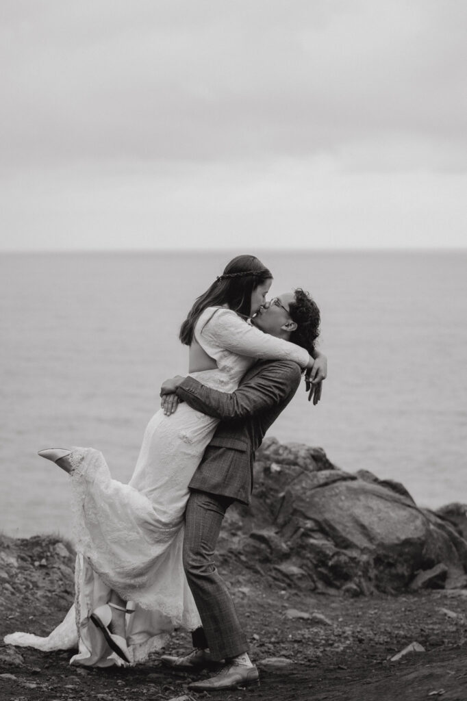 Bride and groom kiss on rocky cliffside during their intimate wedding by the ocean.