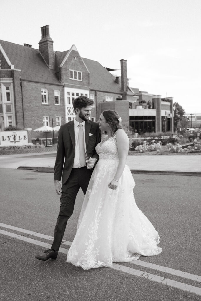 Couple walks hand in hand after their intimate wedding, smiling outside a historic brick venue.