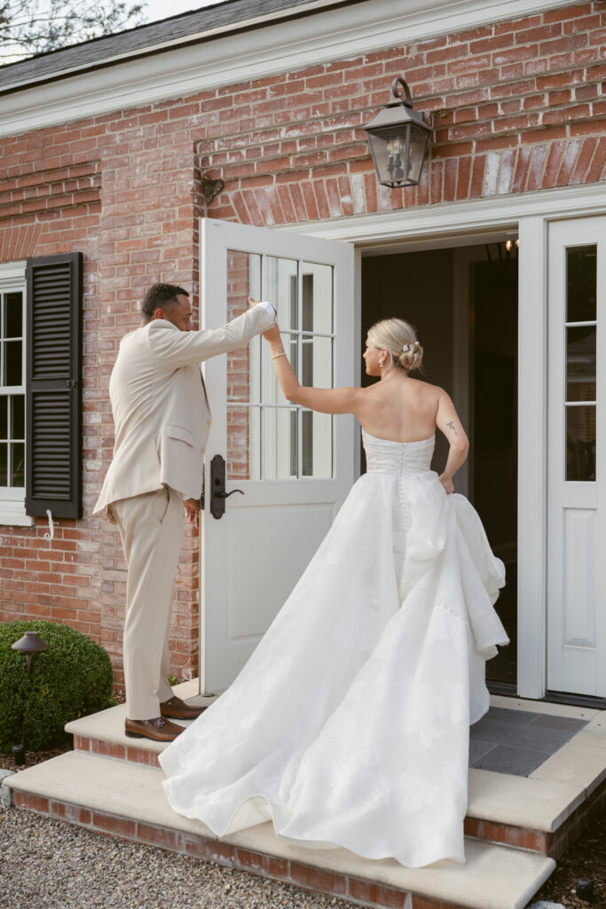 Groom twirls bride as they enter brick venue, her elegant wedding dress flowing behind her.