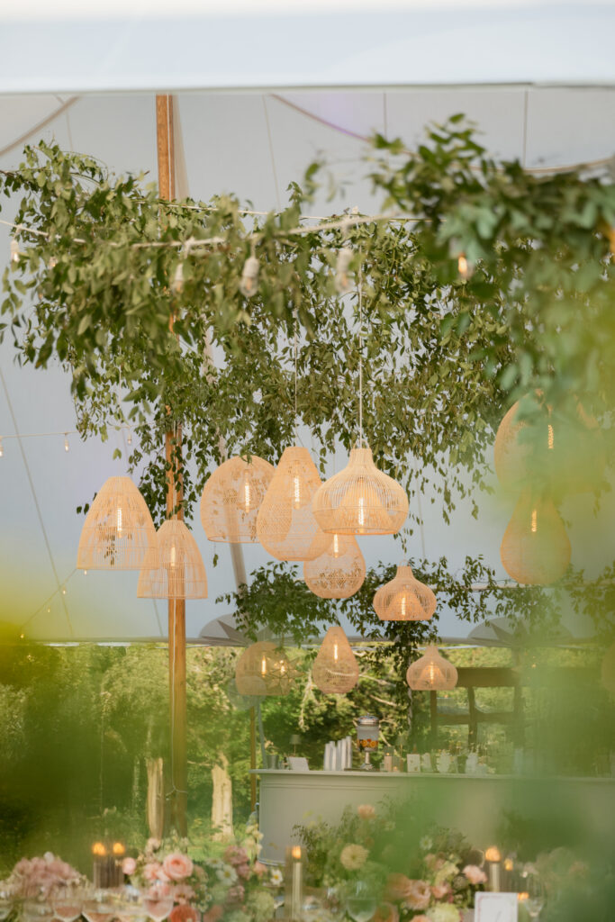 Romantic outdoor wedding bar under a sailcloth tent with woven pendant lights and greenery, beautifully captured by Cincinnati wedding photographers.