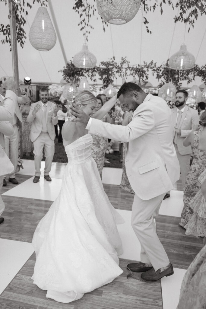 Black and white photo of bride and groom dancing joyfully under tented reception, surrounded by guests—emotional moment captured by Cincinnati wedding photographers.