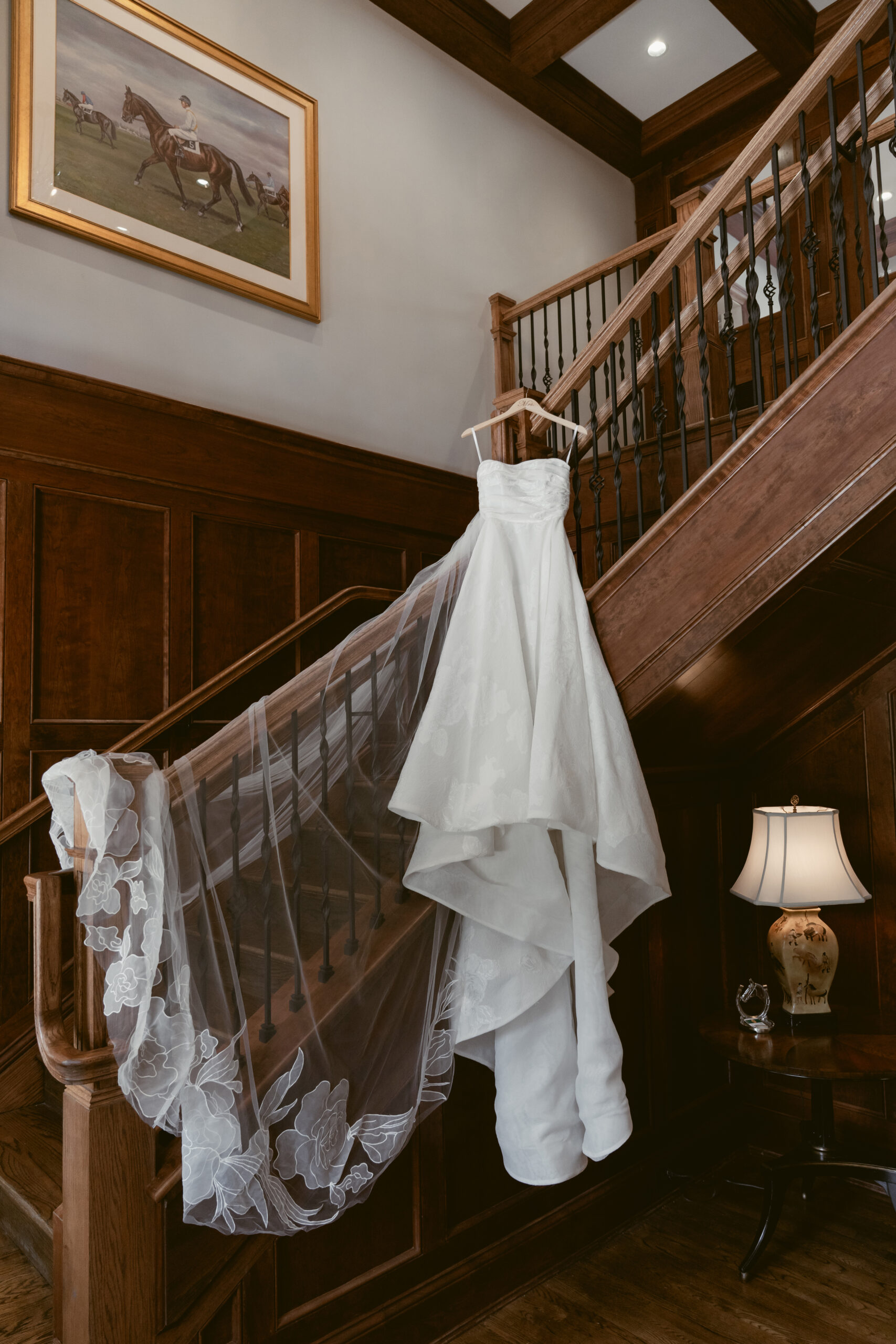 Elegant white wedding dress with floral veil draped over a wooden staircase in classic venue.