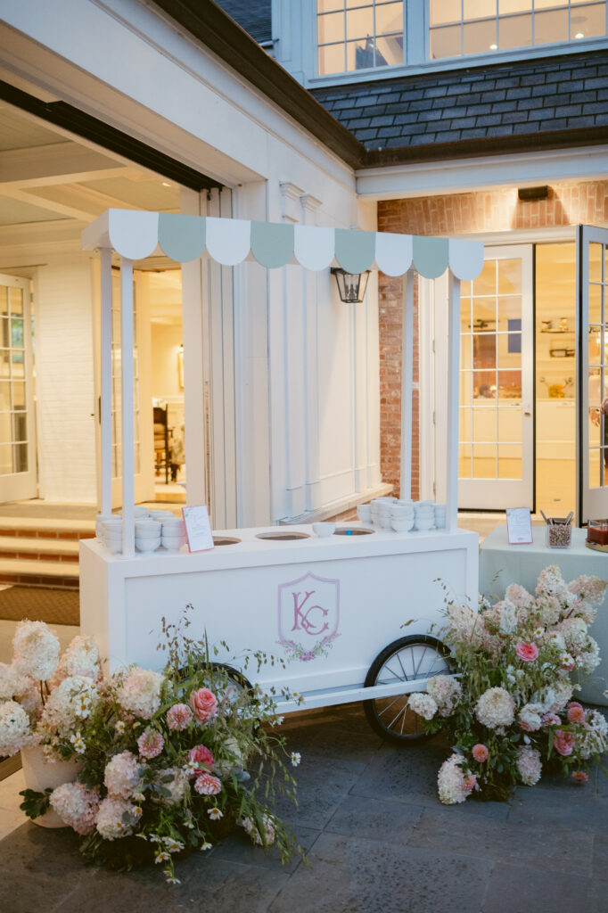 Charming wedding dessert cart with green and white canopy, custom crest, and surrounded by lush floral arrangements—Wedding at Meshewa House