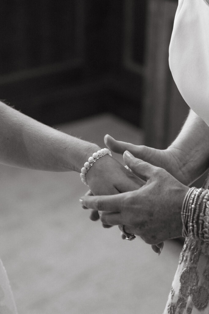 Black and white close-up of mother and bride holding hands, showing delicate pearl bracelet- Wedding at Meshewa House