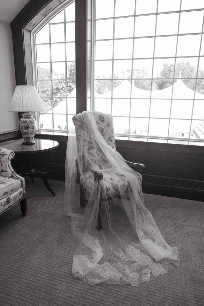 Bridal veil draped over a floral armchair in front of large windows with tented views outside.
