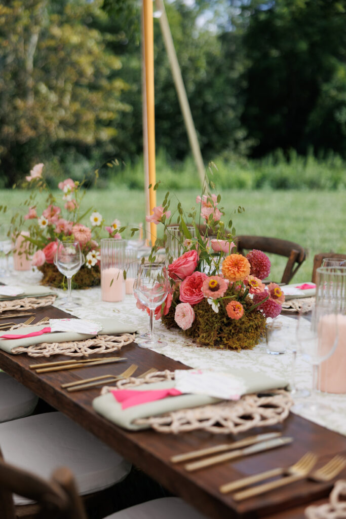 Close-up of a beautifully set outdoor reception table featuring bright floral centerpieces, woven placemats, and gold flatware.