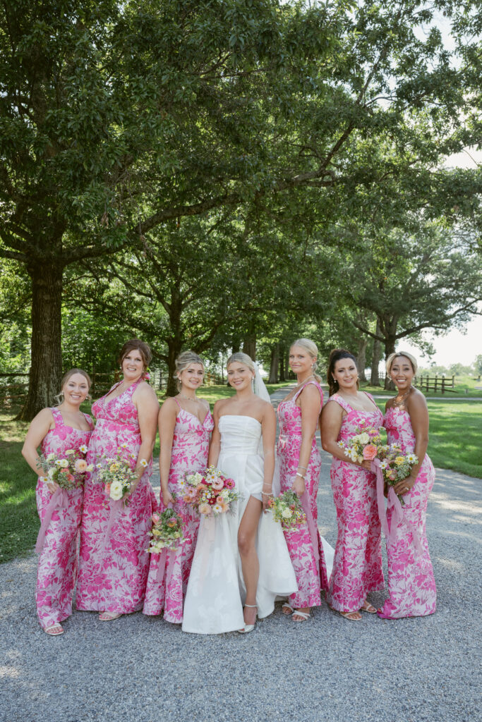 Bride and bridesmaids in vibrant pink dresses pose outdoors- Wedding at Meshewa House