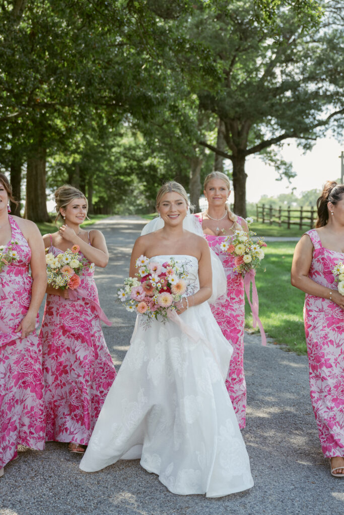 Bride walks confidently with bridesmaids in matching pink floral dresses, holding pastel garden bouquets - Wedding at Meshewa House