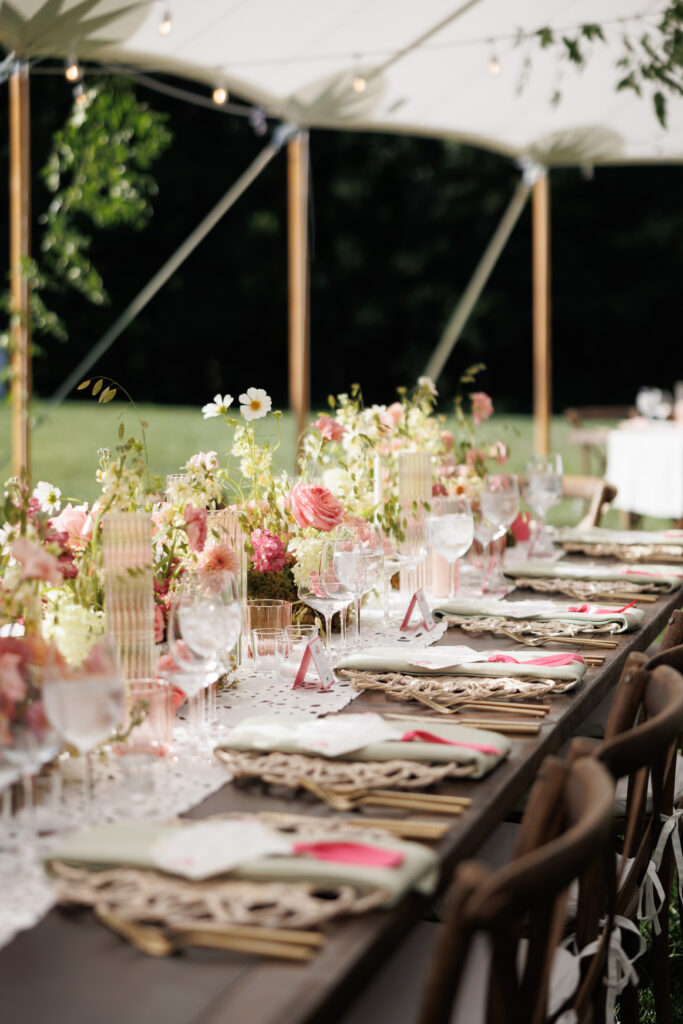 Elegant outdoor wedding reception table under a sailcloth tent, styled with blush pink and ivory florals, rattan chargers, green napkins, and gold flatware—captured by Cincinnati wedding photographers.