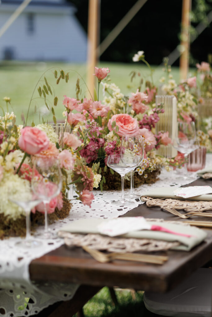 brown wooden table with glassware with stunning pipnk and cream floral table arrangements