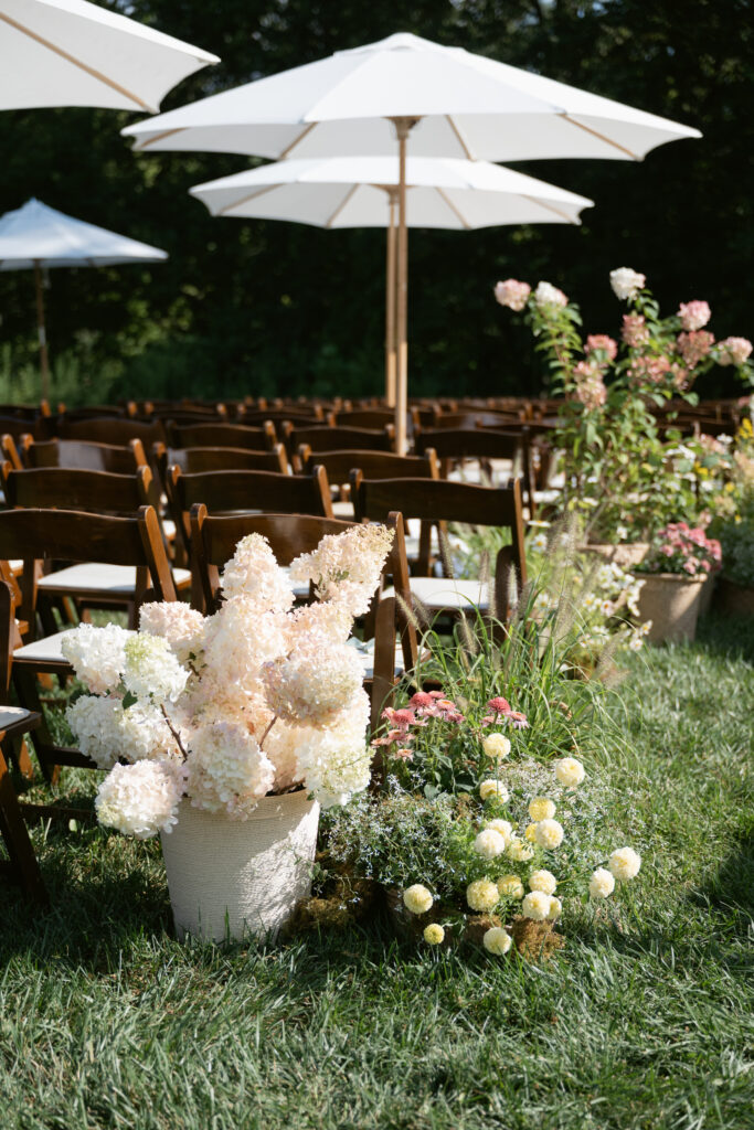Ceremony aisle lined with hydrangeas and garden blooms under white umbrellas on a sunny day - Wedding at Meshewa House