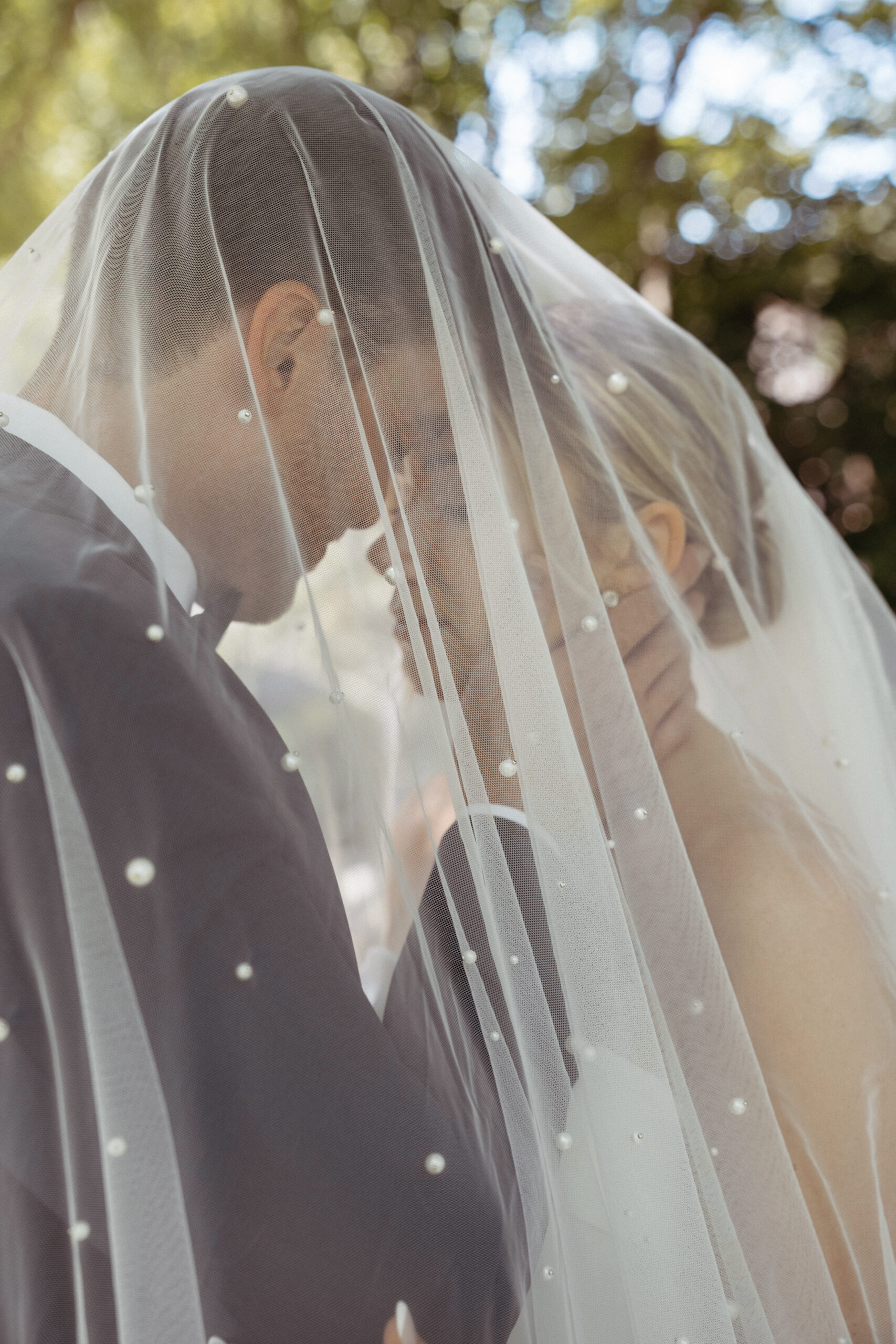 bride and groom holding eachother close underneath the brides veil